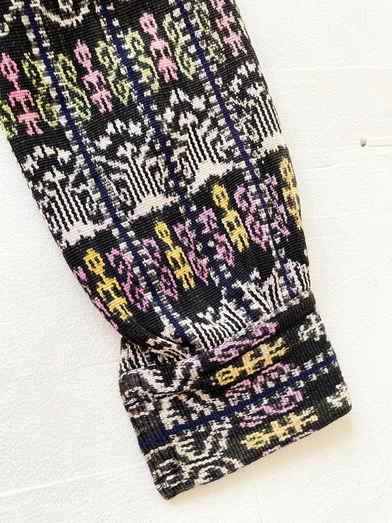 Puede incluir: Primer plano del pu&ntilde;o de una manga de tejido tejido con estampado negro, blanco, rosa y amarillo.