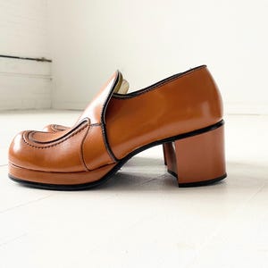 May include: Brown leather platform shoes with a chunky heel. The shoes have a pointed toe and a decorative seam detail.