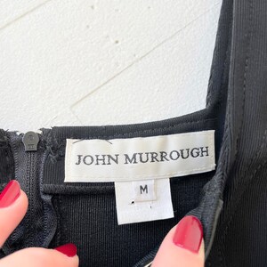 Może przedstawiać: Czarna metka odzieżowa z białym tekstem "JOHN MURROUGH" i białą metką rozmiaru z napisem "M".