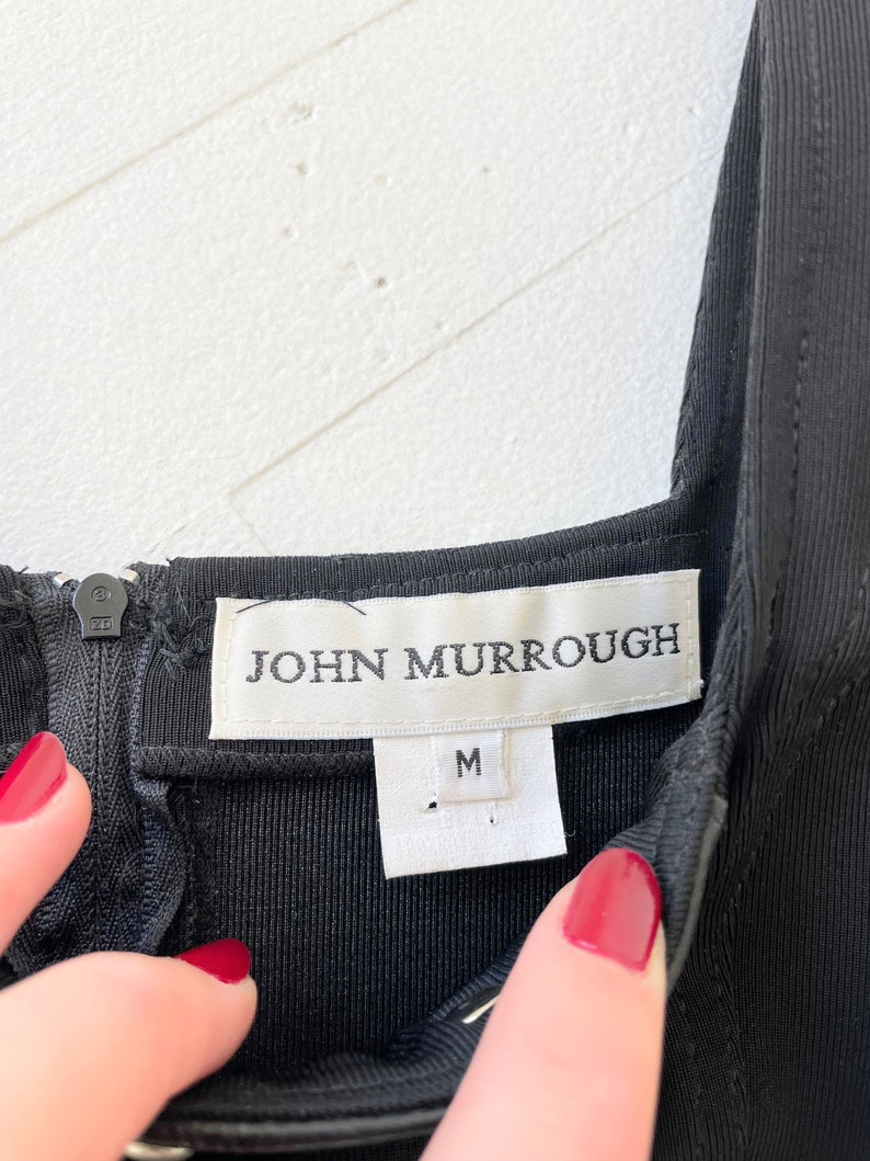 Może przedstawiać: Czarna metka odzieżowa z białym tekstem "JOHN MURROUGH" i białą metką rozmiaru z napisem "M".
