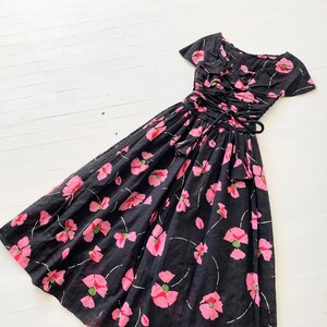 Peut inclure: Une robe noire &agrave; imprim&eacute; floral rose et taille cintr&eacute;e. La robe a des manches courtes et un col &agrave; volants.