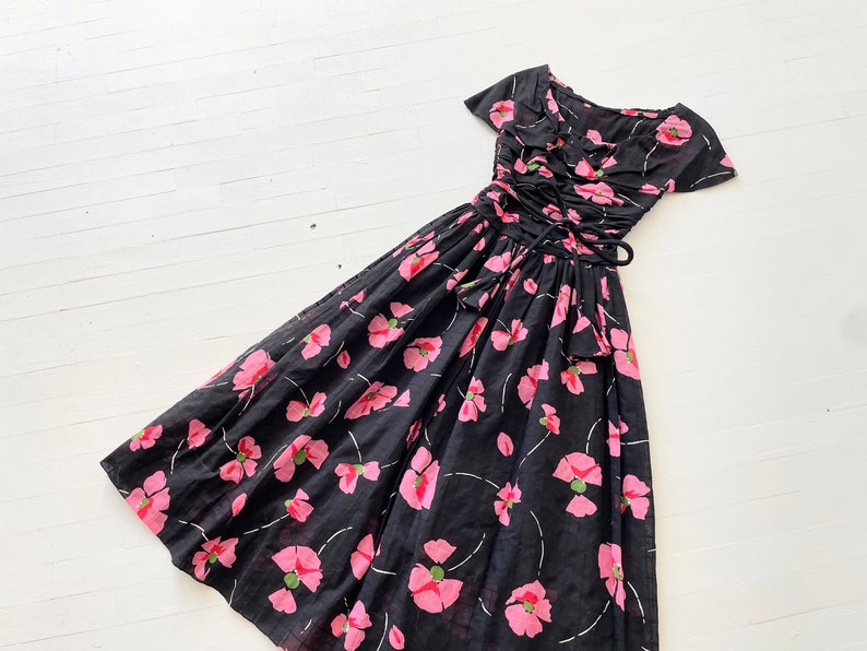 Peut inclure: Une robe noire &agrave; imprim&eacute; floral rose et taille cintr&eacute;e. La robe a des manches courtes et un col &agrave; volants.