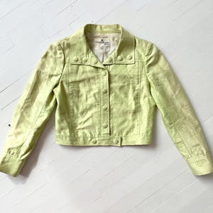 Puede incluir: Chaqueta verde claro con botones y mangas largas. La chaqueta presenta un patr&oacute;n texturizado y un cuello. Los botones redondos coinciden con el color de la chaqueta. La chaqueta es de estilo corto.