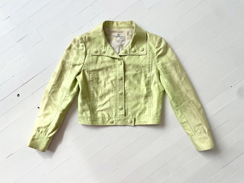 Puede incluir: Chaqueta verde claro con botones y mangas largas. La chaqueta presenta un patr&oacute;n texturizado y un cuello. Los botones redondos coinciden con el color de la chaqueta. La chaqueta es de estilo corto.