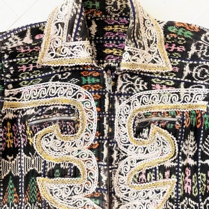 Puede incluir: Una chaqueta con estampado negro y blanco con bordados dorados y blancos. La chaqueta tiene cierre de cremallera y cuello alto.