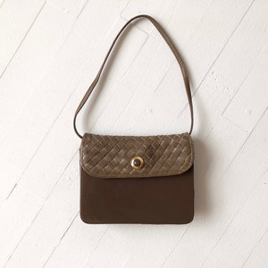 May include: A brown leather shoulder bag with a woven flap and a gold button closure.