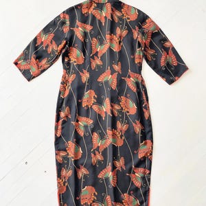 May include: A black dress with a mandarin collar and short sleeves. The dress is covered in a pattern of orange and brown butterflies on a black background. The dress has a red trim around the edges.