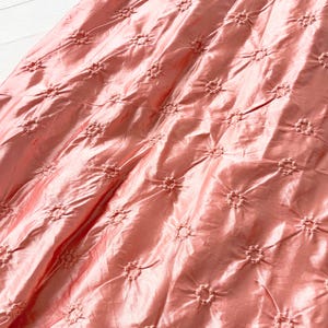 May include: A close-up of a pink fabric with a delicate floral pattern. The fabric has a subtle sheen and a soft, flowing texture.