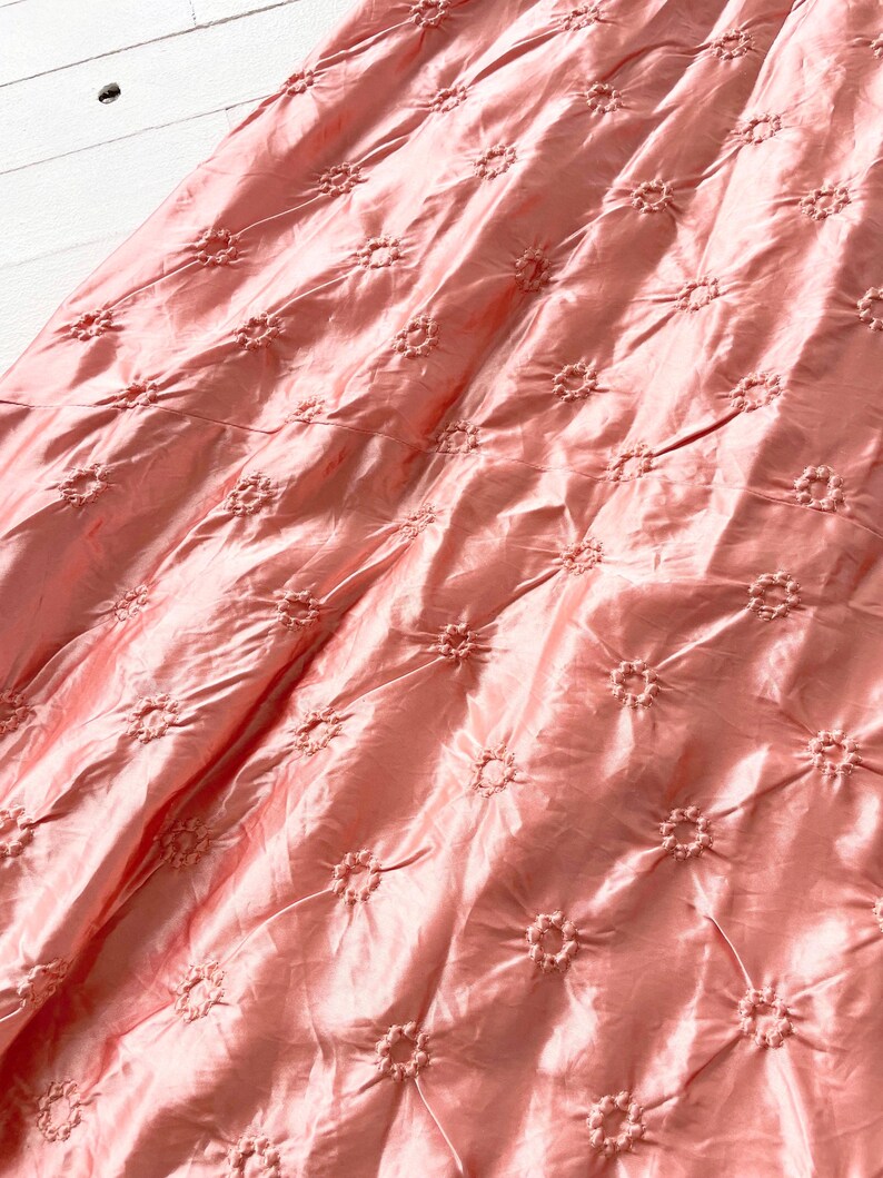 May include: A close-up of a pink fabric with a delicate floral pattern. The fabric has a subtle sheen and a soft, flowing texture.