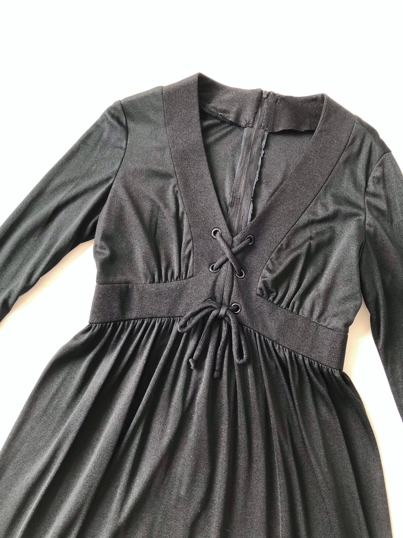 May include: A black long-sleeved dress with a V-neck and a lace-up detail at the bodice.