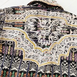 Puede incluir: Tejido tejido en blanco y negro con acentos coloridos y bordados blancos intrincados. El bordado presenta un dise&ntilde;o de p&aacute;jaro estilizado con acentos dorados.