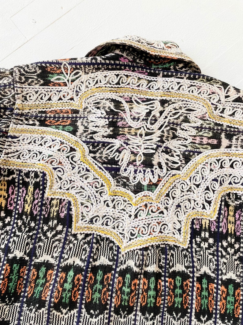 Puede incluir: Tejido tejido en blanco y negro con acentos coloridos y bordados blancos intrincados. El bordado presenta un dise&ntilde;o de p&aacute;jaro estilizado con acentos dorados.