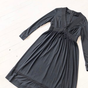May include: A black long-sleeved dress with a V-neck and a lace-up detail at the neckline. The dress has a gathered skirt and a scalloped hem.