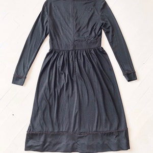 May include: A black long-sleeved dress with a round neckline and a zipper down the back. The dress has a gathered skirt and a lace trim at the hem.