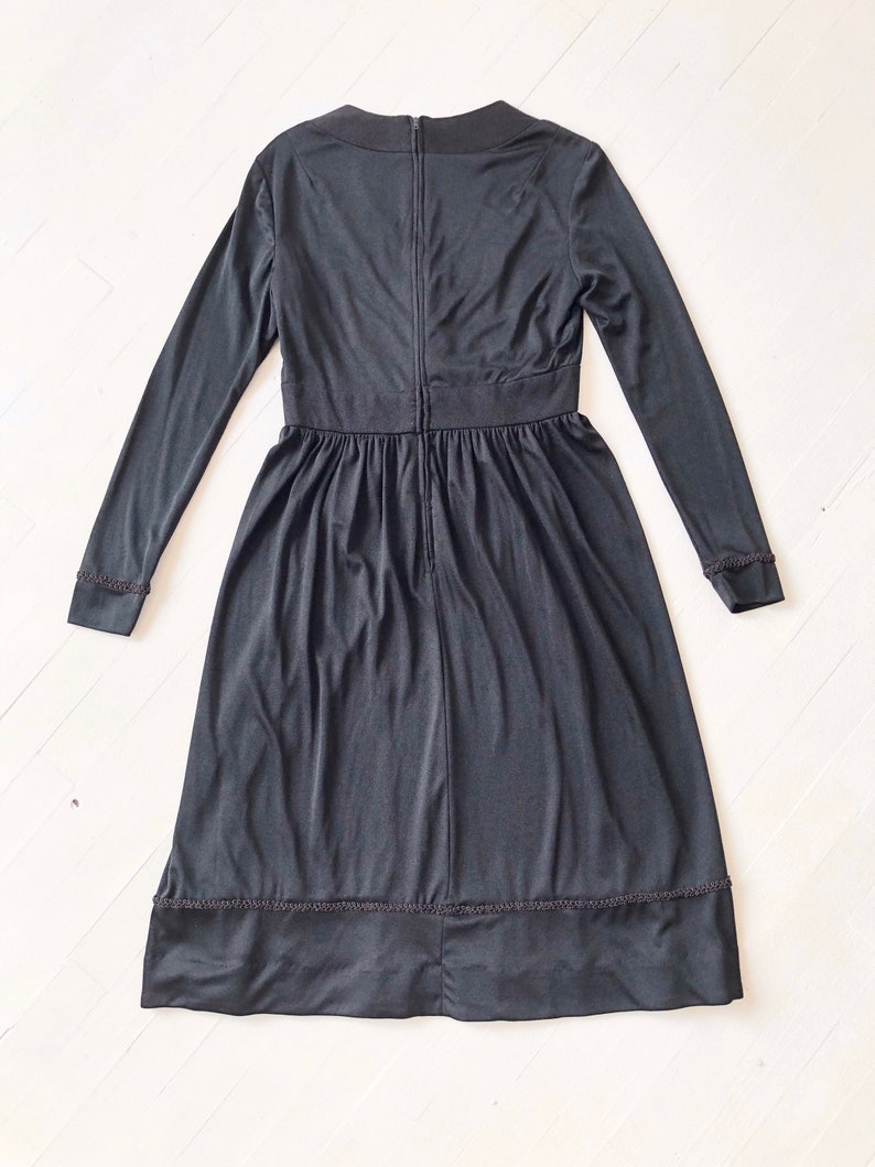 May include: A black long-sleeved dress with a round neckline and a zipper down the back. The dress has a gathered skirt and a lace trim at the hem.