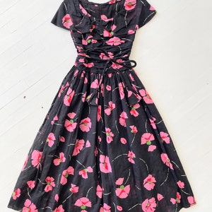 Peut inclure: Une robe vintage noire &agrave; imprim&eacute; floral rose. La robe a un corsage ajust&eacute; avec un d&eacute;collet&eacute; en c&oelig;ur et une jupe ample. La robe est cintr&eacute;e &agrave; la taille par un ruban noir.