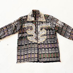 Puede incluir: Una chaqueta negra con un patr&oacute;n geom&eacute;trico colorido y bordados blancos. La chaqueta tiene cuello y mangas largas.