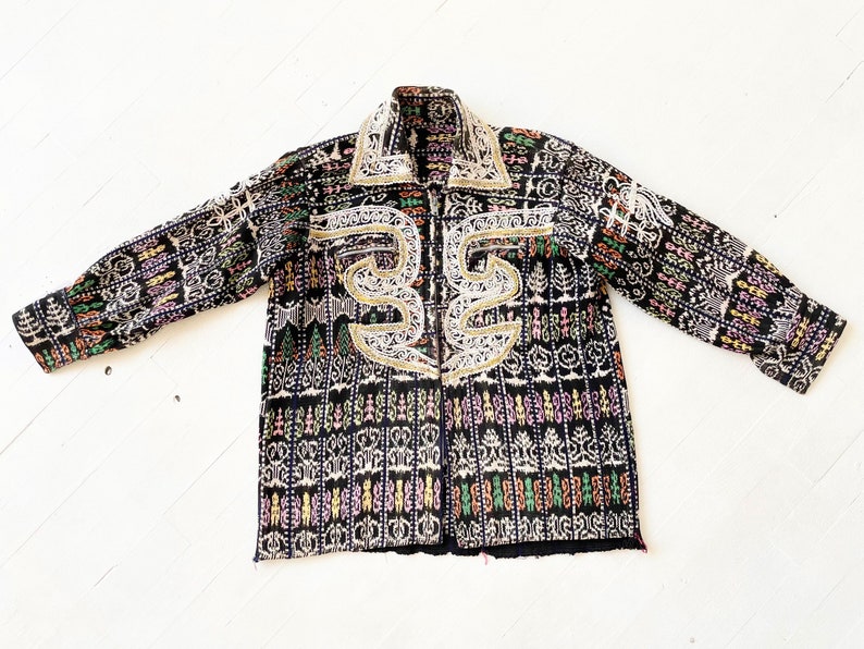 Puede incluir: Una chaqueta negra con un patr&oacute;n geom&eacute;trico colorido y bordados blancos. La chaqueta tiene cuello y mangas largas.
