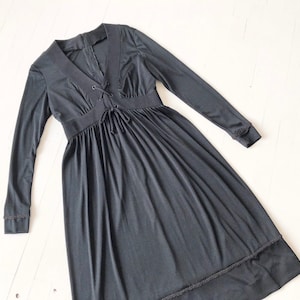 May include: A long-sleeved black dress with a V-neck and a lace-up detail at the neckline. The dress has a gathered skirt and a lace trim at the hem.
