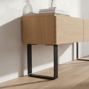 Puede incluir: Un mueble de madera clara de forma rectangular, con un veteado natural. Está sostenido por patas de metal negro de sección cuadrada. El diseño es moderno y minimalista, adecuado para un salón o dormitorio. El mueble mide aproximadamente 150 cm de largo.
