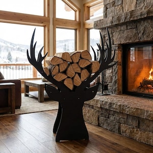 May include: A black metal deer head-shaped log holder filled with firewood. The holder is in front of a stone fireplace and hardwood floor. The antlers extend upwards, and the firewood is stacked between them. The room has large windows with a view of a snowy landscape.