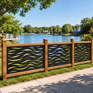 May include: A fence featuring three rectangular panels with a black metal insert displaying a repeating horizontal wave pattern, framed by vertical and horizontal light brown wooden posts and rails, positioned along a grassy area near a lake.