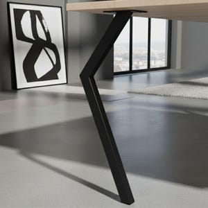 Op de afbeelding: Een moderne houten tafel met een lichtkleurig blad en een zwart metalen poot. De poot heeft een uniek hoekig ontwerp, wat een eigentijdse uitstraling geeft. De tafel staat in een lichte kamer met uitzicht op de stad door een groot raam.