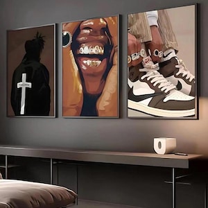 May include: Set of three framed art prints. One features a person in a black jacket with a cross and the word "FORGIVEN". Another shows a close-up of a smiling face with gold teeth. The third depicts a person's legs and sneakers.
