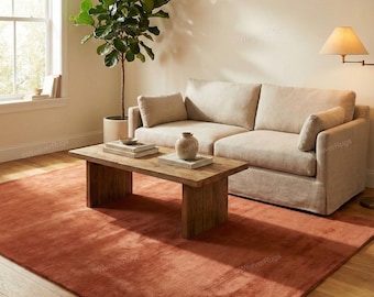 May include: A living room with a rust-coloured rug, a light beige sofa, and a wooden coffee table. A potted plant and a lamp enhance the room's decor. The rug covers a large area of the hardwood floor.