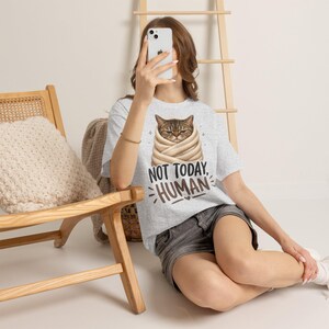 Könnte beinhalten: Ein hellgraues Kurzarm-T-Shirt mit einer Grafik einer braunen getigerten Katze, die in eine beige Decke eingewickelt ist. Unter der Katze steht der Text NOT TODAY, HUMAN in schwarzer und brauner Schrift, ergänzt durch kleine Stern- und Herzsymbole.