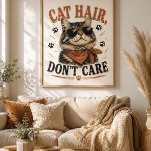 Könnte beinhalten: Ein gerahmter Kunstdruck, der eine getigerte Katze mit schwarzer Fliegerbrille und einem rostfarbenen Halstuch zeigt. Der Text "CAT HAIR, DON'T CARE" ist in einer fetten, abgenutzten Schriftart gedruckt und von kleinen Pfotenabdrücken umgeben.