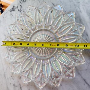 以下が含まれることがあります： 星模様とスカラップ状の縁を持つ、透明で虹色に輝くガラス皿。中央に黄色いメジャーが置かれており、皿の直径が端から端まで約28cmであることを示しています。