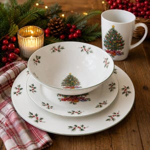 Puede incluir: Un juego de vajilla de cerámica blanca con un patrón de árbol de Navidad y acebo. El juego incluye un plato llano grande, un plato más pequeño, un cuenco hondo y una taza, decorados con hojas verdes y bayas rojas.