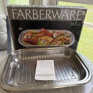 May include: A rectangular stainless steel Farberware roasting pan with a removable wire rack. The pan is positioned in front of its original cardboard packaging, which displays the brand name and a graphic of a prepared seafood and rice dish.