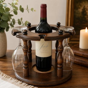 May include: A circular dark brown wooden wine bottle and glass holder featuring a central compartment for one bottle and four slots along the rim for hanging wine glasses. The stand is supported by four turned wooden pillars on a round base.