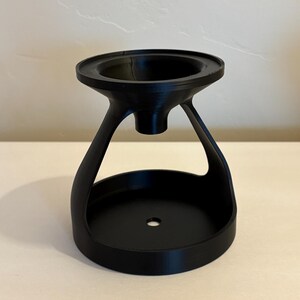 May include: A black, 3D-printed object with a unique design. It features a wide, circular base, a central opening, and a flared top. The object has a modern, minimalist aesthetic and appears to be a decorative or functional item.