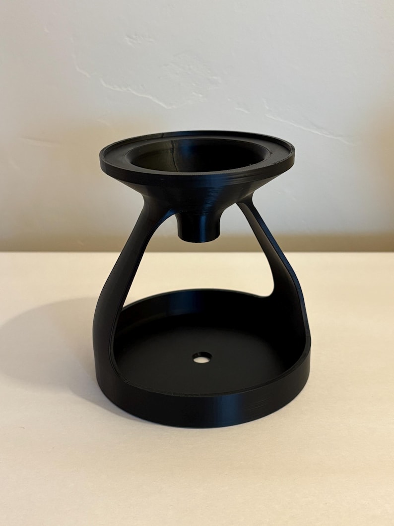May include: A black, 3D-printed object with a unique design. It features a wide, circular base, a central opening, and a flared top. The object has a modern, minimalist aesthetic and appears to be a decorative or functional item.