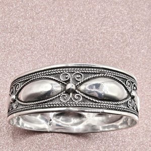 Puede incluir: Una pulsera de plata con un diseño ornamentado. La pulsera presenta tres acentos ovalados y patrones detallados de filigrana y cuerda. La pulsera mide aproximadamente 2,5 cm de ancho.