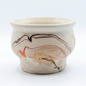 May include: A ceramic planter with a cream-colored base and a marbled design in shades of brown, orange, and black. The planter has a rounded shape with a slightly flared rim, suitable for small plants or succulents.