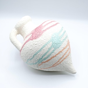 Peut inclure: Un vase en céramique blanc cassé texturé, avec une anse et une base pointue. Le vase est décoré de stries roses, turquoise et pêche. Le vase est incliné sur un fond blanc.