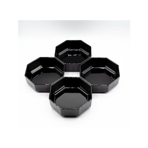 Puede incluir: Cuatro cuencos negros, octagonales, dispuestos en forma de flor. Cada cuenco tiene un acabado brillante y un interior poco profundo. Los cuencos están hechos de un material sólido y son adecuados para servir aperitivos o porciones pequeñas.
