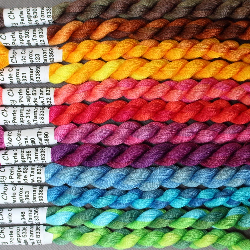 May include: A selection of vibrant embroidery threads in shades of brown, yellow, pink, red, purple, blue, and green. Each skein is carefully wound and labelled, ideal for a range of needlework crafts.