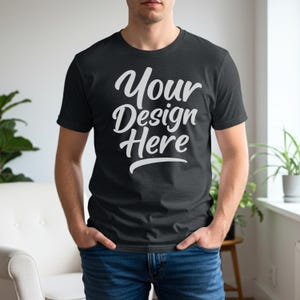 Pu&ograve; includere: Una t-shirt a maniche corte grigio antracite scuro con la scritta bianca Your Design Here stampata in un carattere corsivo in grassetto sul petto. Il capo presenta un classico girocollo e una vestibilit&agrave; standard, abbinato a jeans blu.