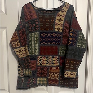 Puede incluir: Un suéter patchwork en tonos burdeos, verde oliva y beige. El suéter presenta un cuello redondo y mangas largas. El diseño está formado por varios patrones y formas geométricas, creando un aspecto único y texturizado.