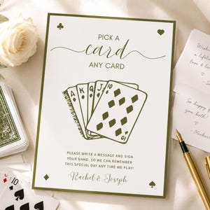 May include: A rectangular white sign with a dark green border featuring the text PICK A CARD ANY CARD and an illustration of playing cards. The sign includes instructions to write a message and sign names, with the names Rachel & Joseph at the bottom.