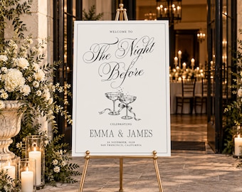 May include: A white rectangular wedding welcome sign on a gold easel featuring black text that reads Welcome To The Night Before, Celebrating Emma & James, 26 November, 2028, San Francisco, California, with a line drawing of two champagne glasses.