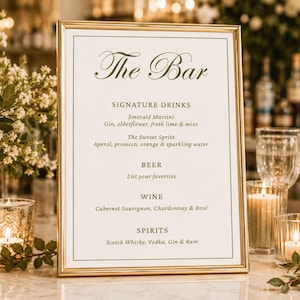 Puede incluir: Un letrero rectangular con marco dorado, fondo blanco y texto en verde oscuro que dice The Bar, Signature Drinks, Emerald Martini, The Sunset Spritz, Beer, Wine y Spirits, enumerando varios ingredientes de cócteles y categorías.