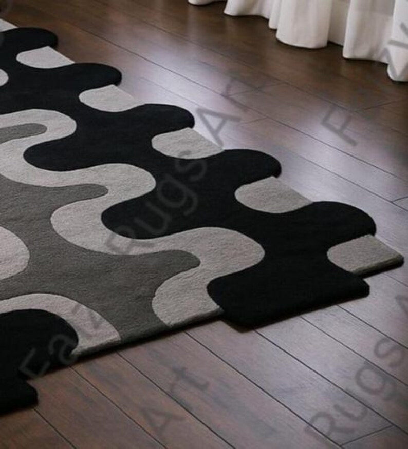 May include: A modern area rug with a unique, flowing design. The rug features a pattern of black, gray, and light gray organic shapes. The rug is placed on a dark wood floor, adding a touch of contemporary style to any room.