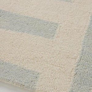 May include: Close-up of a textured rug with a geometric pattern. The rug features alternating bands of light blue and off-white, creating a soft, inviting aesthetic. The fibers appear plush and comfortable.