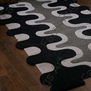 May include: A modern area rug with a wavy pattern in black, gray, and off-white. The rug's design features large, flowing shapes that create a bold visual statement. The rug is placed on a wooden floor.